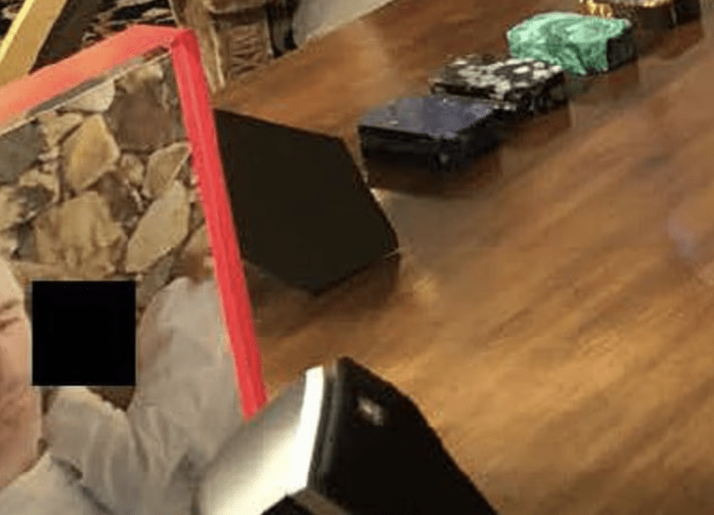 书桌上还有另外两张被遮盖身份的照片，一张在左角，显示一人（疑似未成年人）手臂环抱爱泼斯坦，头部靠在他的肩上。